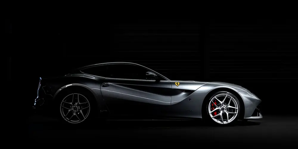 Silver Ferrari grand tourer in profile under dramatic studio lighting
