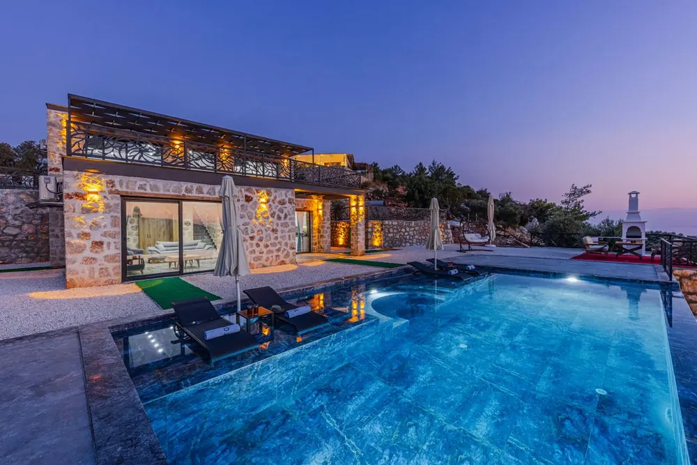 Luxury stone villa with an illuminated infinity pool at dusk